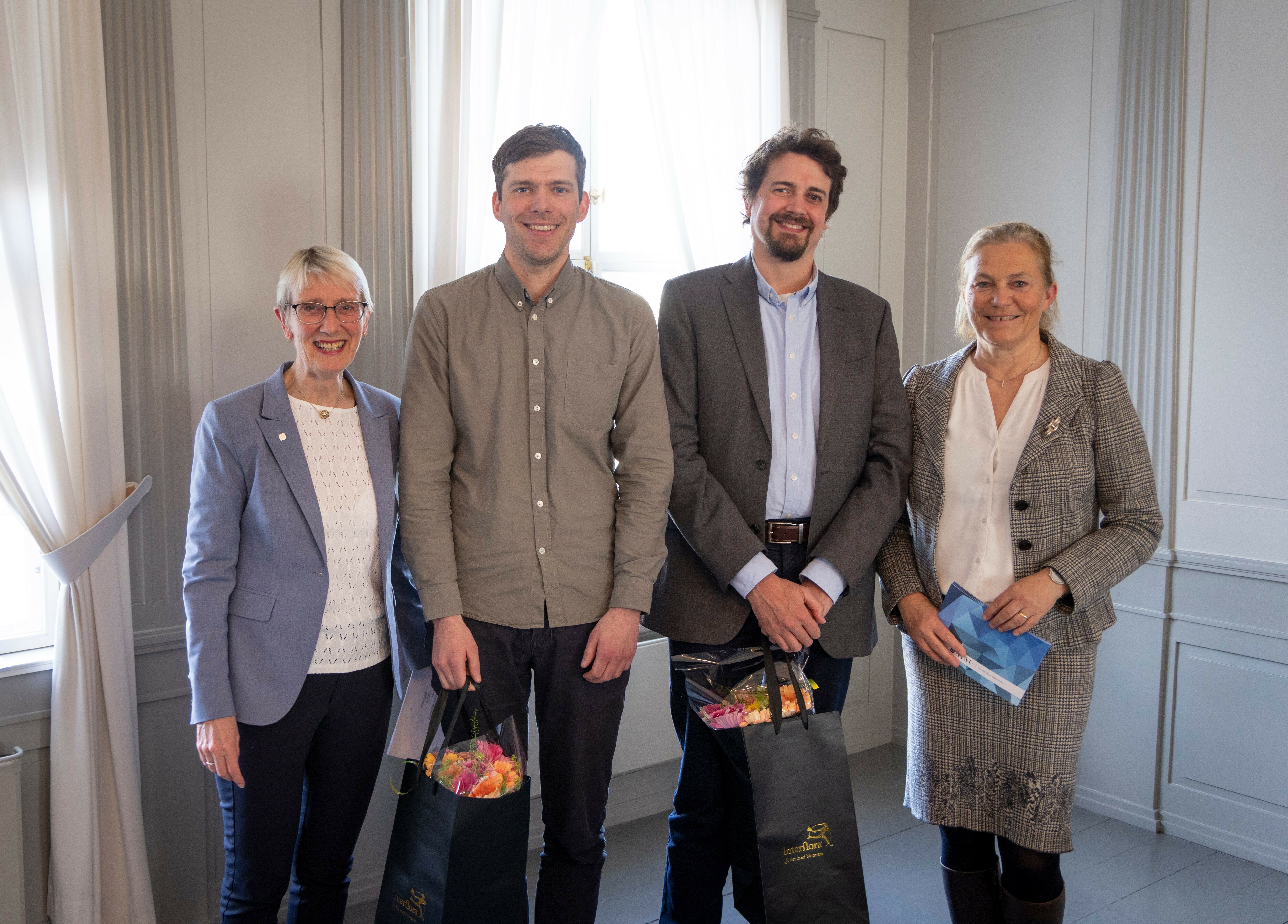 NTNU-rektor Anne Borg, førsteamanuensis Marius Korsnes, seniorforsker Mads Dahl Gjefsen og SINTEF-konsernsjef Alexandra Bech Gjørv står på rekke og smiler mot kamera. Korsnes og Gjefsen holder hver sin blomsterbukett. Foto.